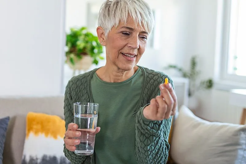 Senior woman taking daily vitamins with a glass of water